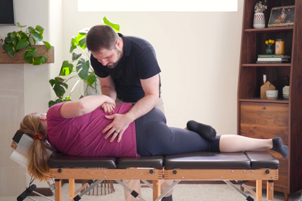 Dr. Mason Stewart of New Leaf Chiropractic adjusts a female patient at home.