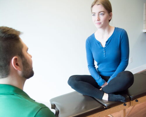 Dr. Mason Stewart discussing treatment with a female patient seated on a chiropractic table.