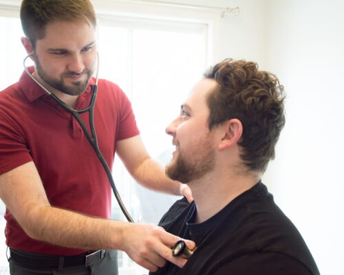 Dr. Mason Stewart uses a stethoscope to listen to the lungs of a male patient.