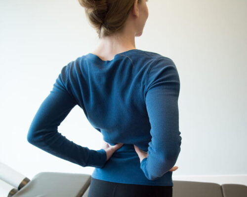 A female patient uses her hands to stretch her back.